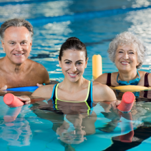 Three adults in a swimming pool with floating noodles